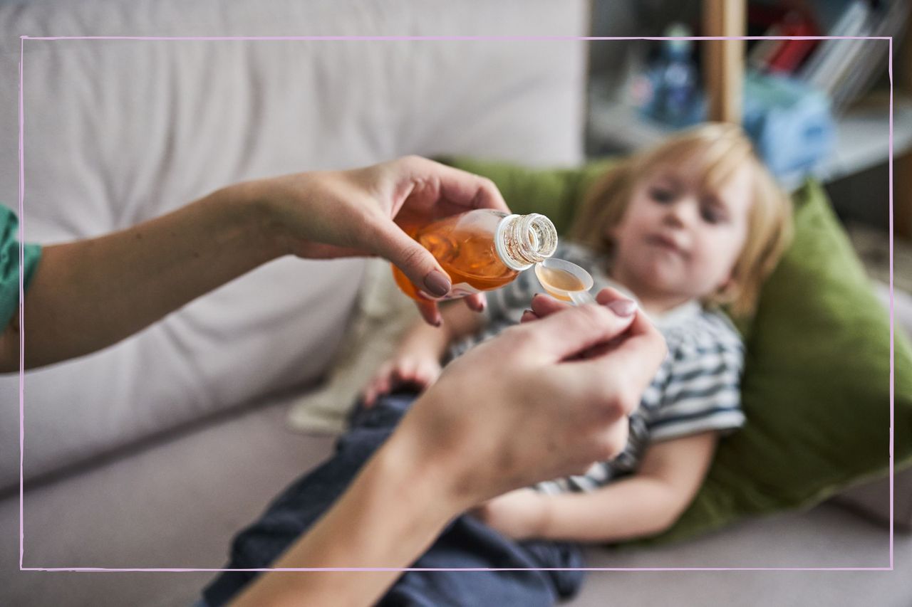 A close up of a woman puring cough medicine onto a spoon with a child lying down in the background