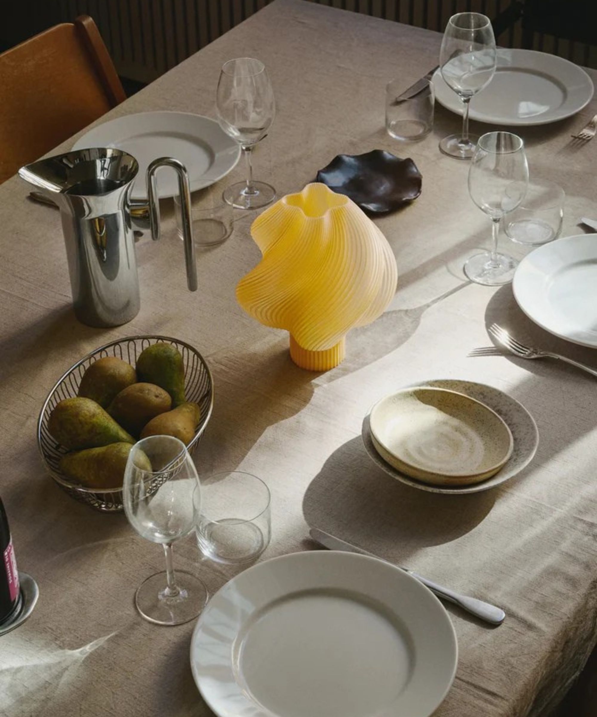 dining table set with linen tablecloth, white plates, extra bowl, chrome basket of pears, chrome jug, wine glasses and water glasses and a Cr&amp;egrave;me Atelier Soft Serve lamp