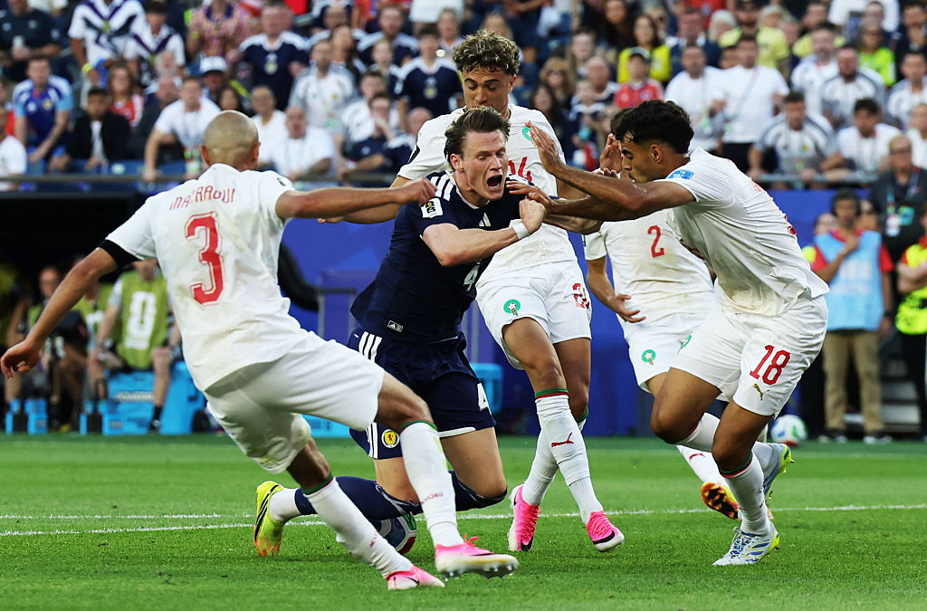 FOXBOROUGH, UNITED STATES - JUNE 19: Scotland's Scott McTominay goes down under a challenge from Morocco's Chadi Riad and Noussair Mazraoui during a 2026 FIFA World Cup Group C match between Scotland and Morocco at the Boston Stadium, on June 19, 2026, in Foxborough, United States. (Photo by Craig Williamson/SNS Group via Getty Images)