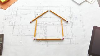 architect plans with house shape constructed using pencils on top of plans