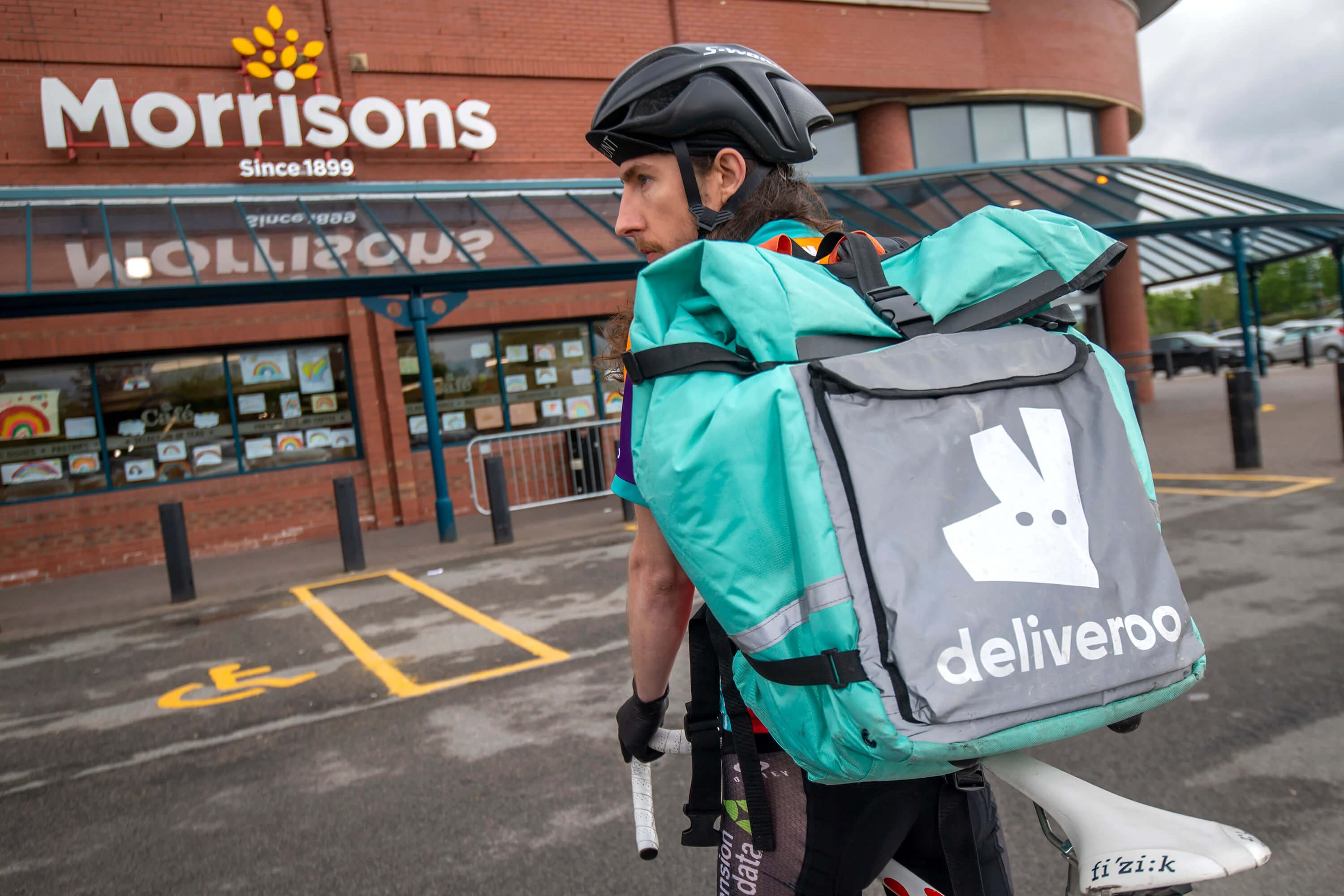 An image showing a deliveroo bicycle driver in front of a Morrisons store