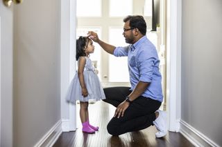 Father kneeling to measure young daughter's height on the door frame at home