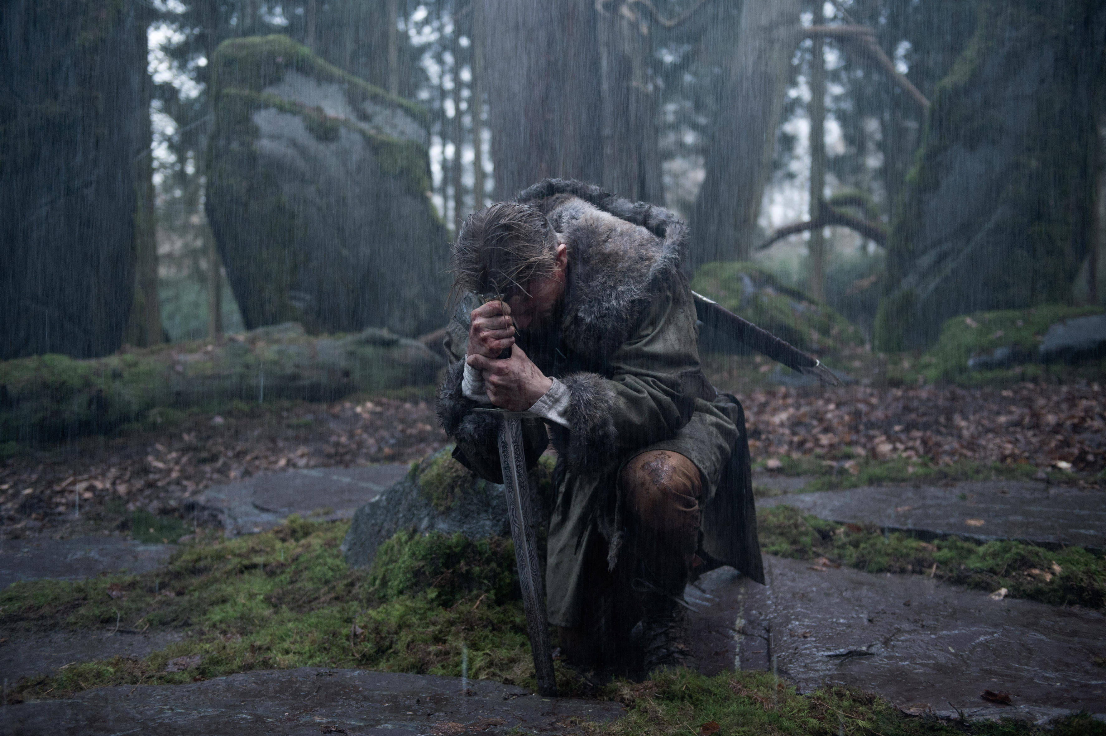 Charlie Hunnam como el Rey Arturo se arrodilla mientras sostiene su espada en un bosque en King Arthur Legend of the Sword
