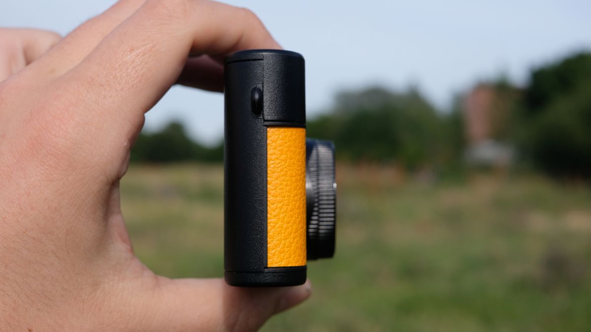 Photograph of man's hand holding Camp Snap 2 digital camera, in yellow colorway, side view facing right
