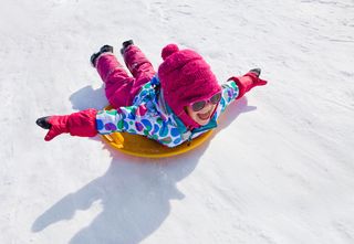 A little girl goes sliding down a snowy hill on a saucr