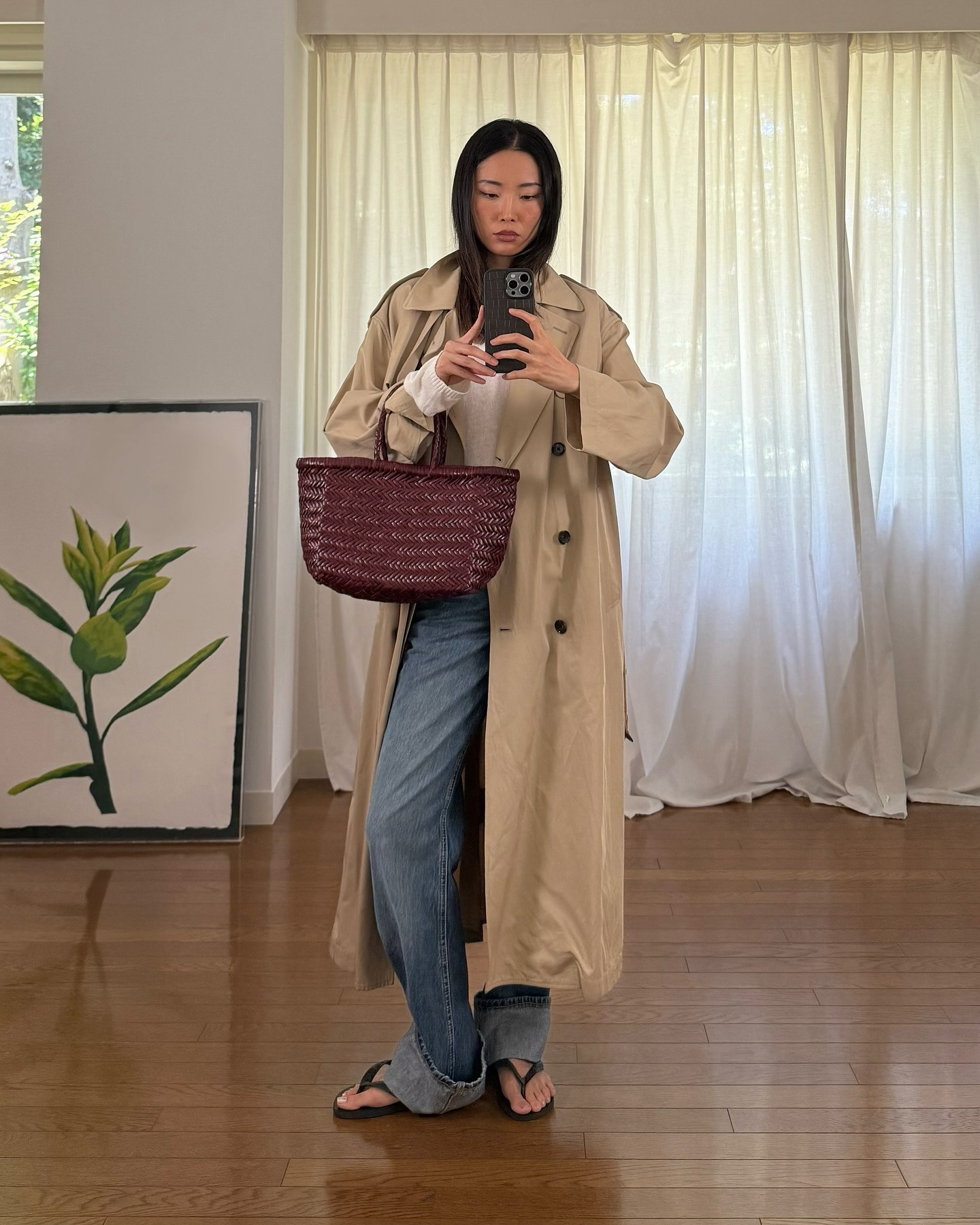 Woman wears trench coat, white top, blue cuffed jeans, black flip flops and burgundy leather bag