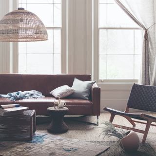 A living room with a brown leather sofa with slim arms, a rattan pendant lamp shade and a lounge woven chair to the side