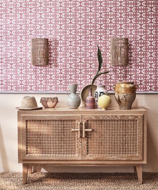 A hallway wallpaper idea with pink geometric wallpaper and rattan sideboard