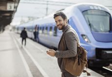 Photo of a smiling businessman texting on his mobile phone at train station