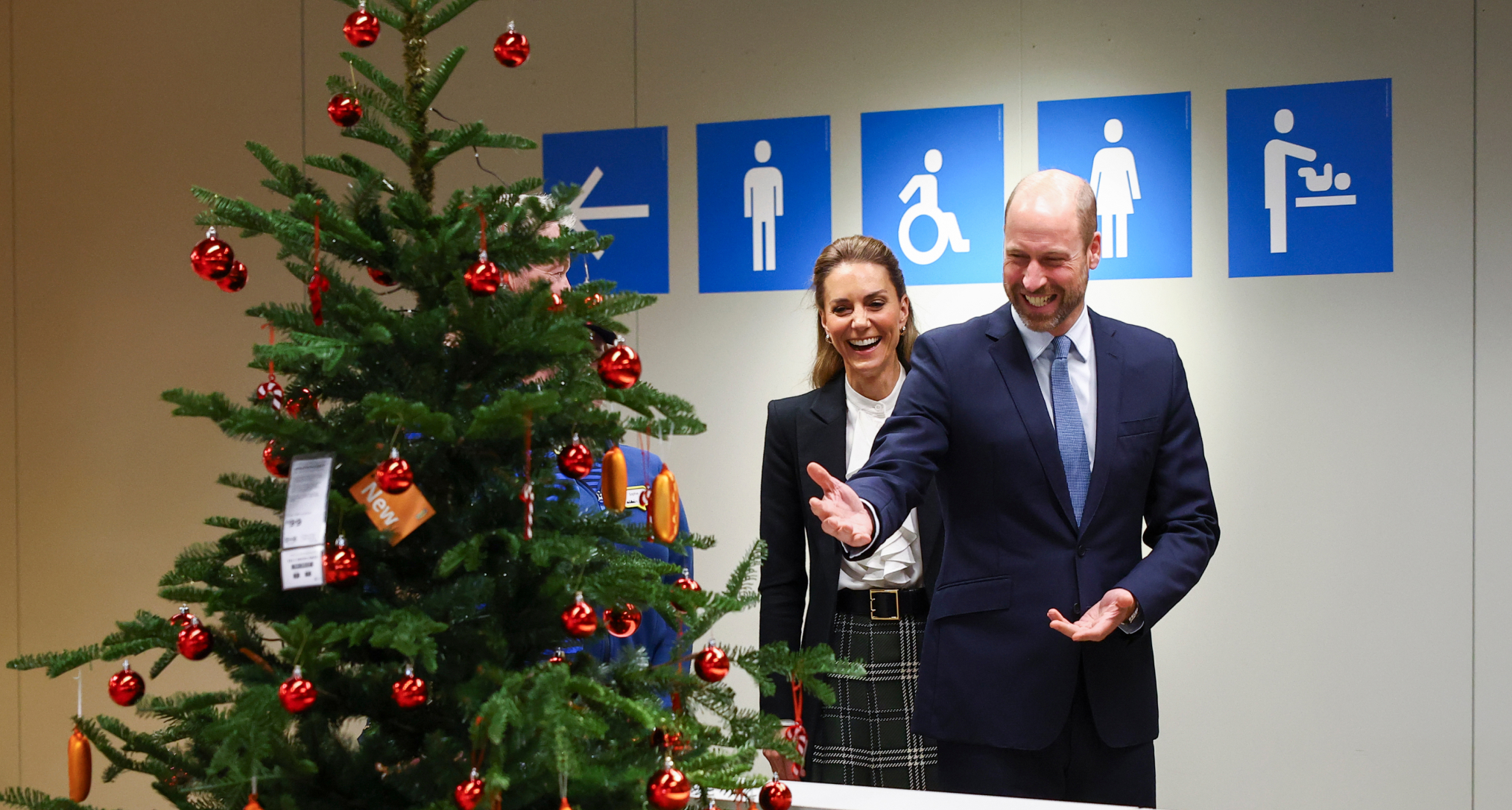 Prince William and Princess Kate standing in front of a Christmas tree and laughing