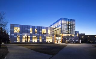 The Taylor Institute of Teaching and Learning at the University of Calgary. The photo was taken from the outside at night. We see the entrance and the rest of the building that's covered in panoramic windows. The lights are on.