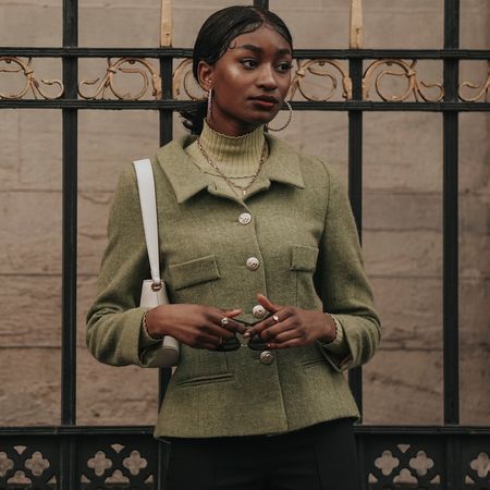 a paris fashion week attendee wearing a green fitted blazer gold hoop earrings turtleneck sweater and white shoulder bag 