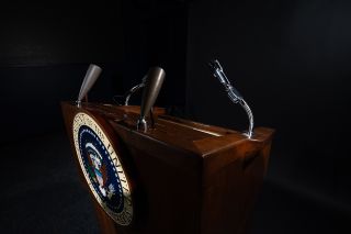 a wooden lectern with three microphone stands sits against a black background.