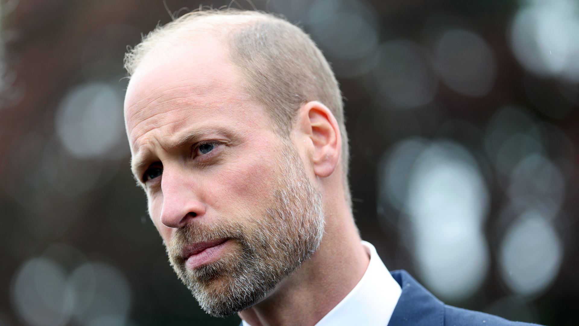 Prince William wearing a white shirt and blue jacket looking stern