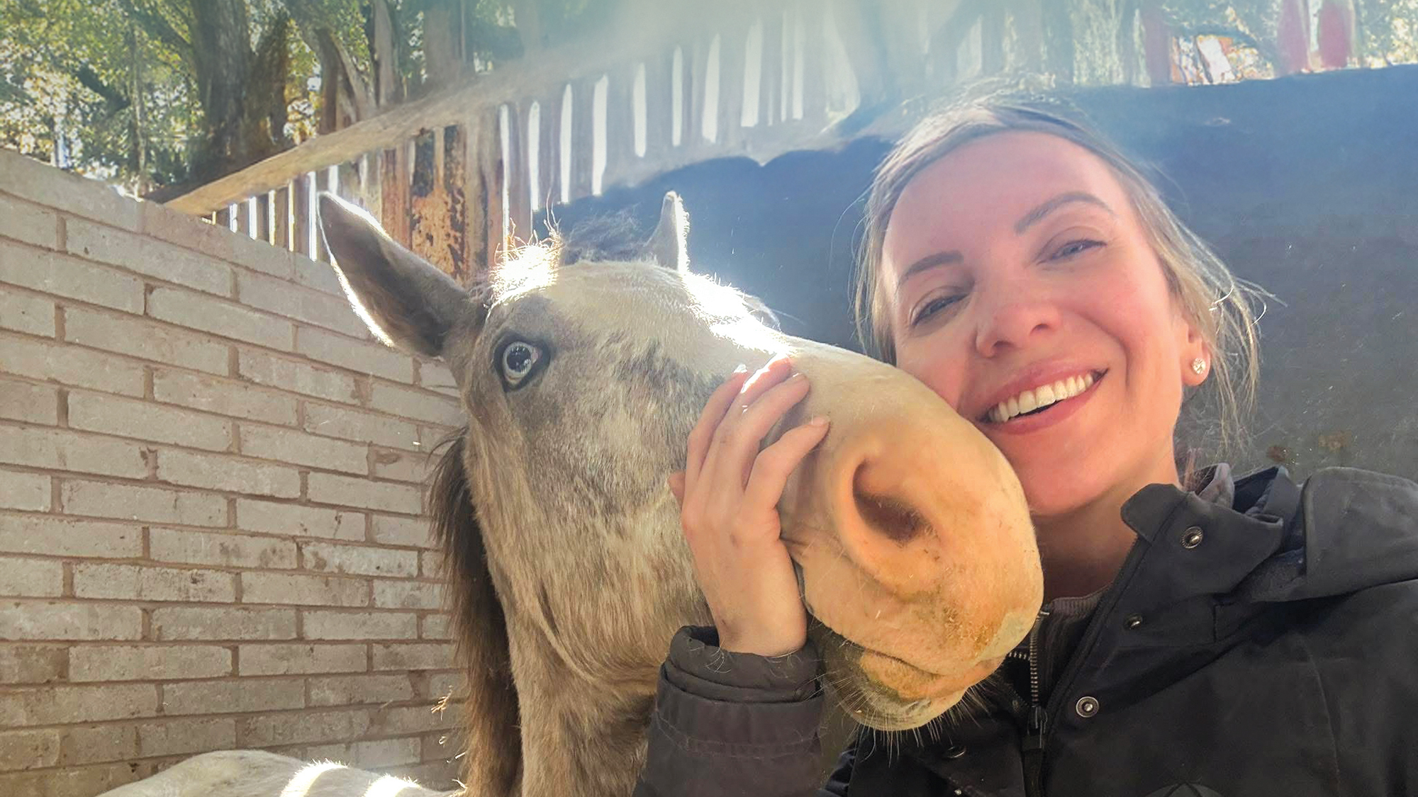 Vet Emily Westwood stands beside a mottle coloured horse with a wall eye with her hand around the horse's muzzle