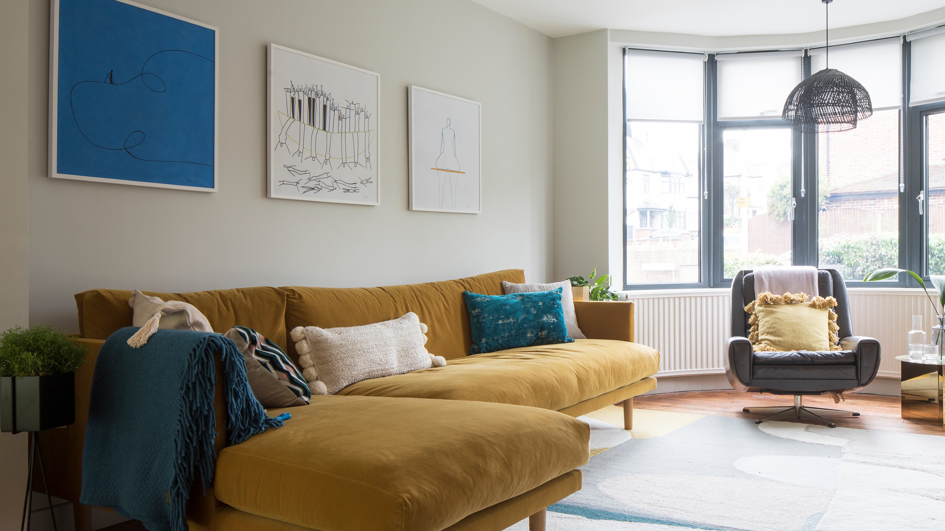 A living room with large windows painted in a neutral shade with a contrasting chaise sofa in mustard yellow velvet