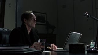 Screenshot from the movie Alien vs. Predator. A man is sitting at a desk in front of a laptop. He is wearing a black robe and has a glass of water in his hand.