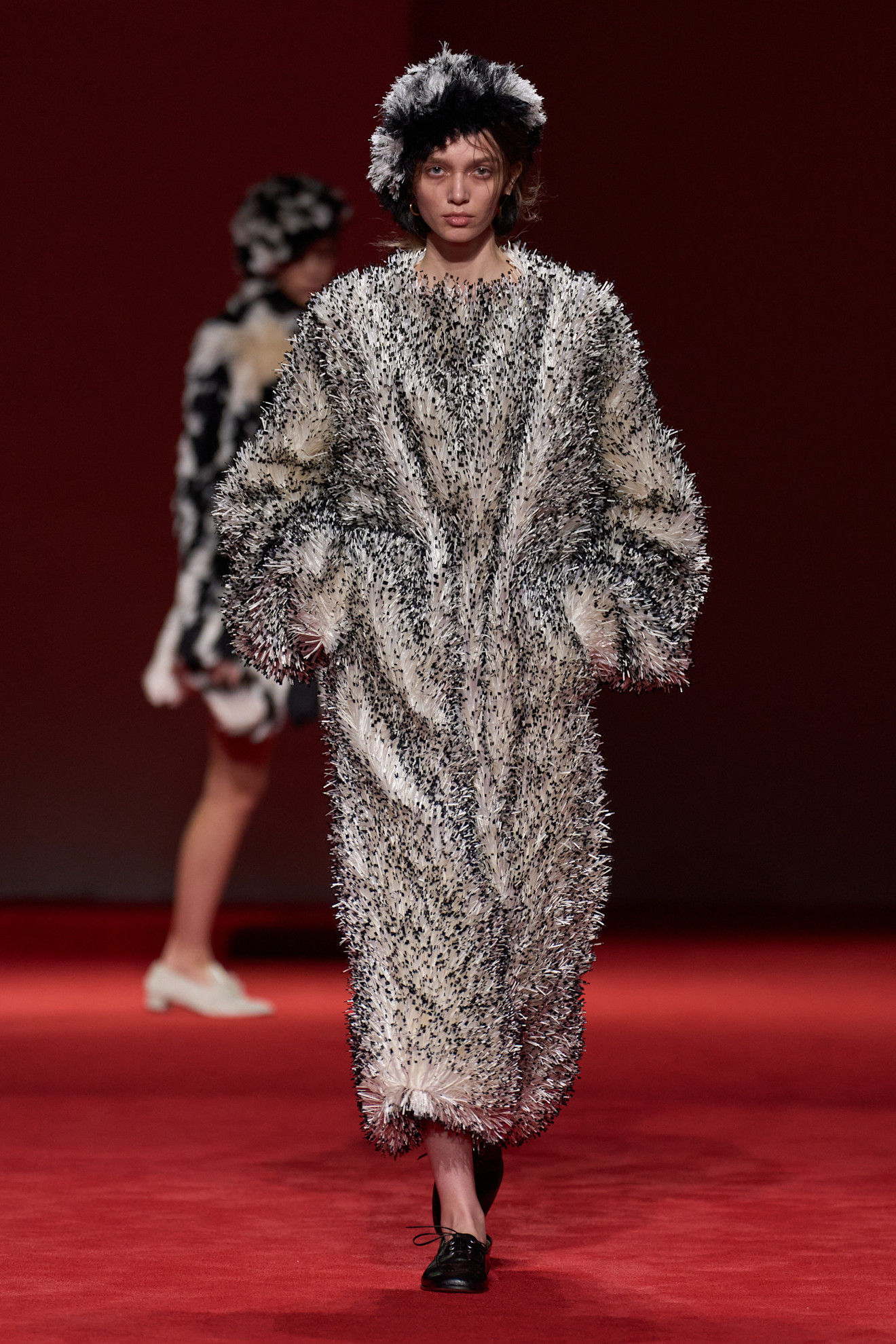 A model walking in the F/W 26 Bottega Veneta show during Milan Fashion Week wearing a beaded fringe coat and hat.