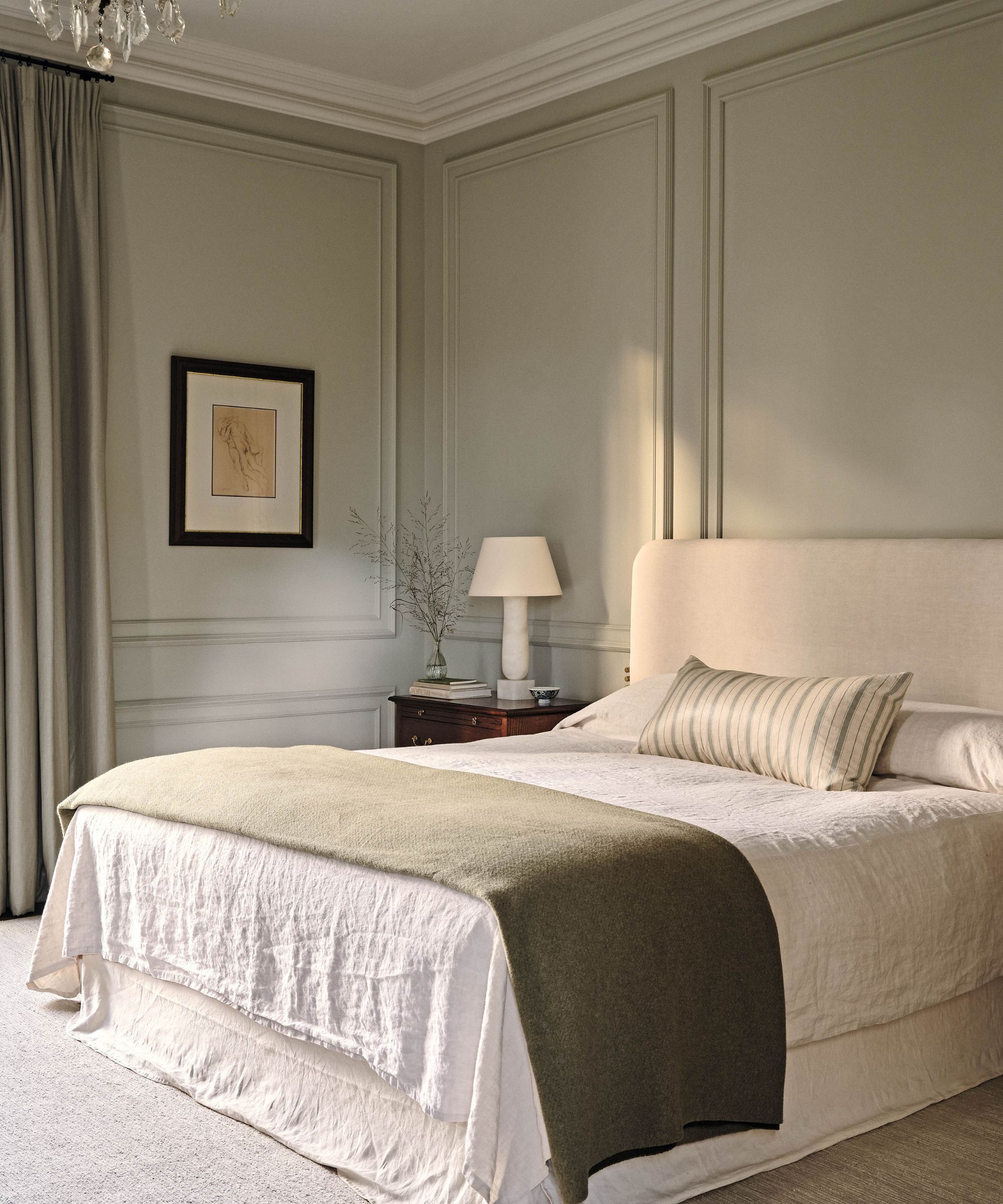 a light sage green painted bedroom with wall moldings, a large neutral bed styled with loose linens, a green throw, and striped bolster pillow