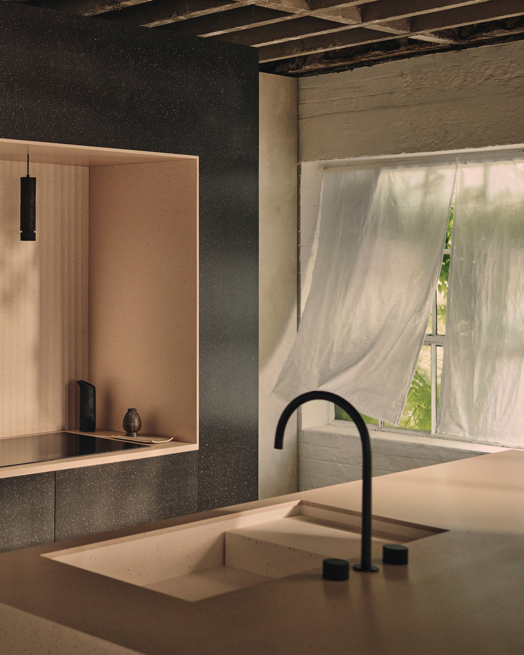Image of a minimalist, industrial kitchen with black walls and tan countertops. There is a window with thin linen curtains blowing in it.