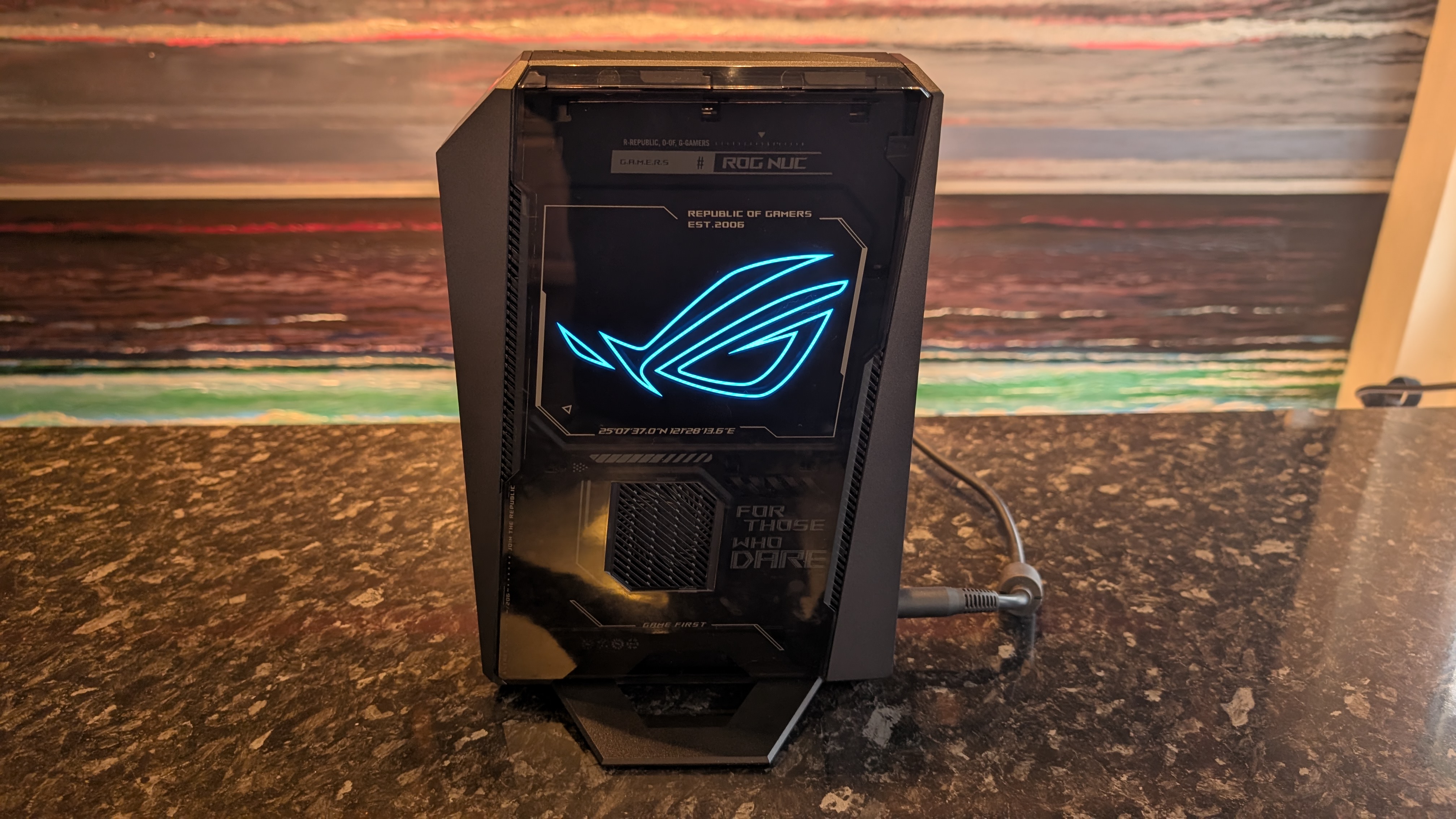 The Asus ROG NUC photographed on a dark marbled worksurface with a painted sunset in the background.