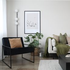 A living room with a light sofa and a black lounge chair and a slim floor lamp behind it