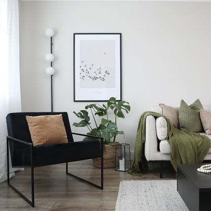 A living room with a light sofa and a black lounge chair and a slim floor lamp behind it