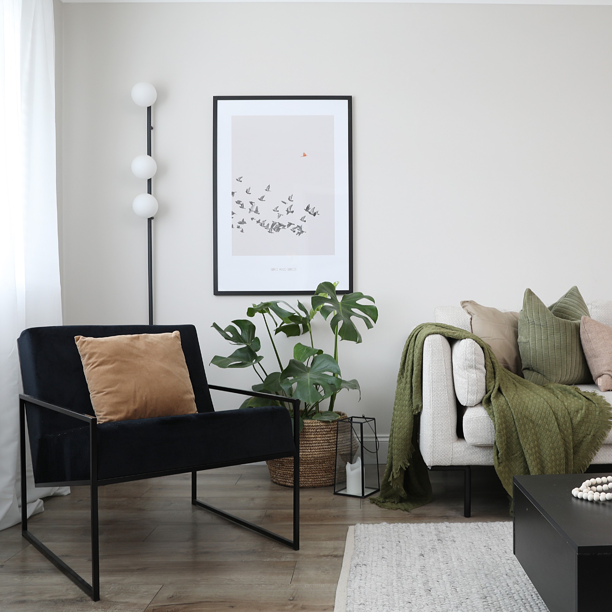 A living room with a light sofa and a black lounge chair and a slim floor lamp behind it