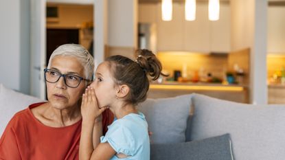 A little girl whispers something to her grandmother, who looks concerned.