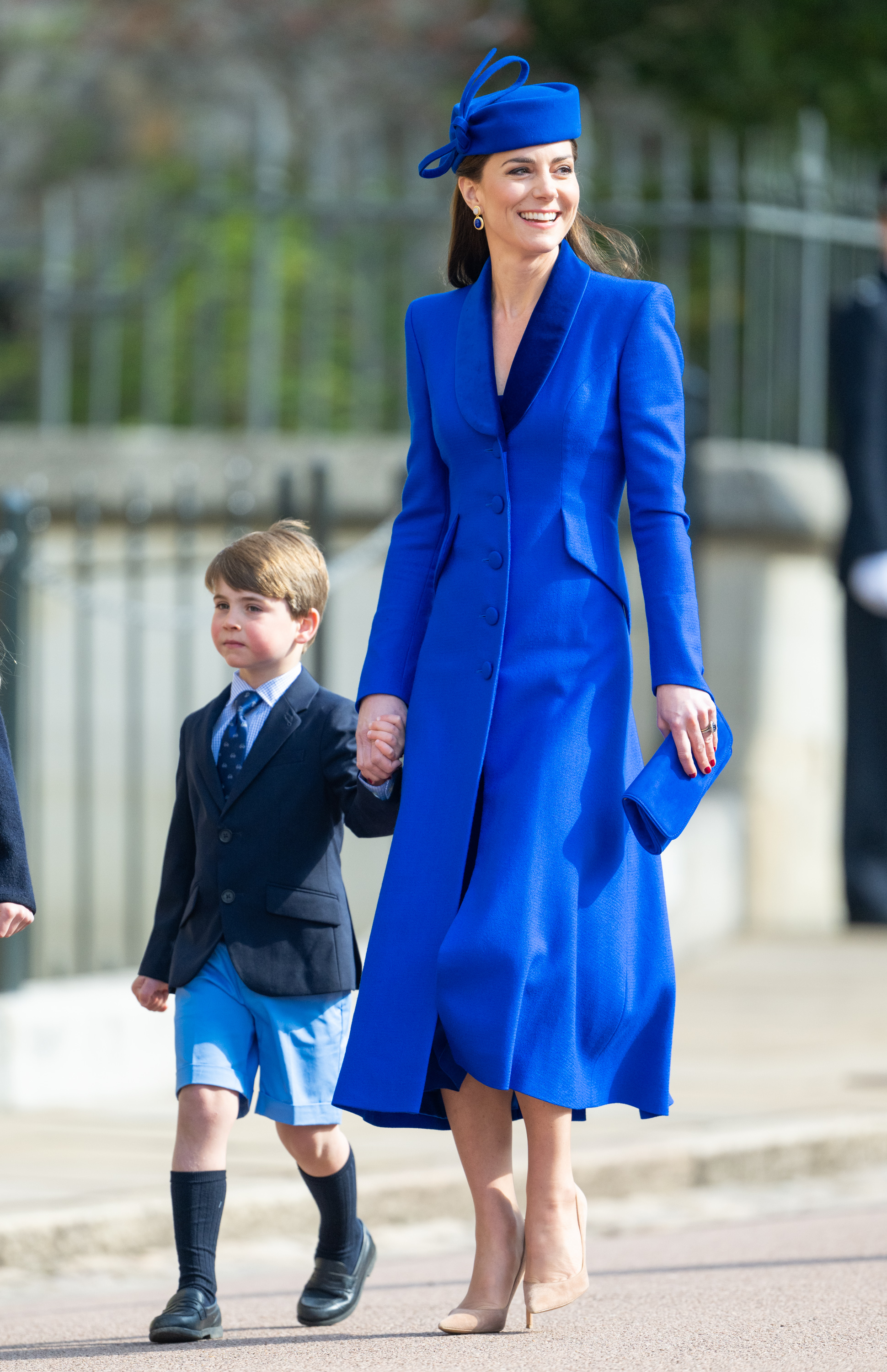 Princess Kate wearing a blue coat and hat holding hands with Prince Louis