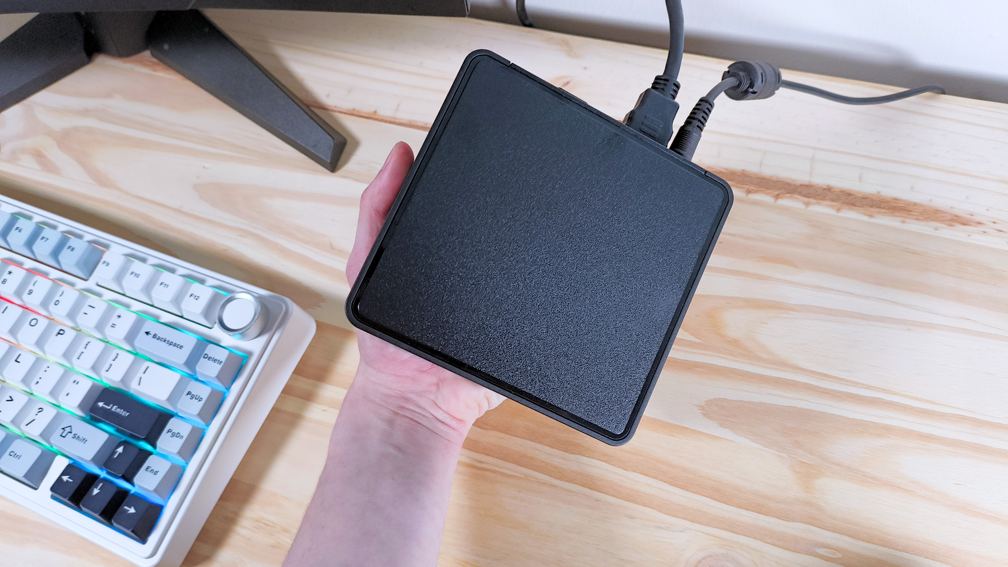 A hand holding up the Asus NUC 14 Pro mini PC in front of a keyboard and monitor