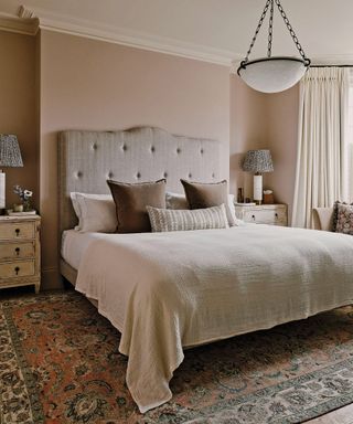 bedroom with pale pink walls and patterned rug and tall fabric headboard