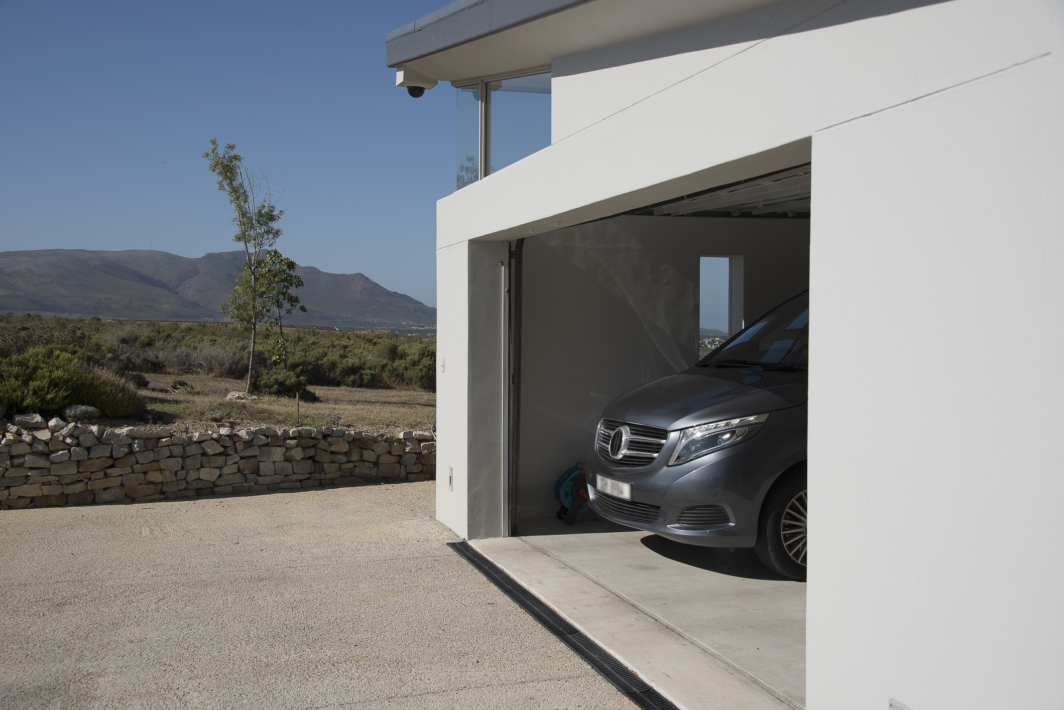A garage in a modern home houses a luxury car. There are mountains in the distance.