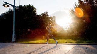 Woman running on sidewalk in the early morning sunlight with light glinting off the camera, one way that the best time to sleep and wake up changes for some people