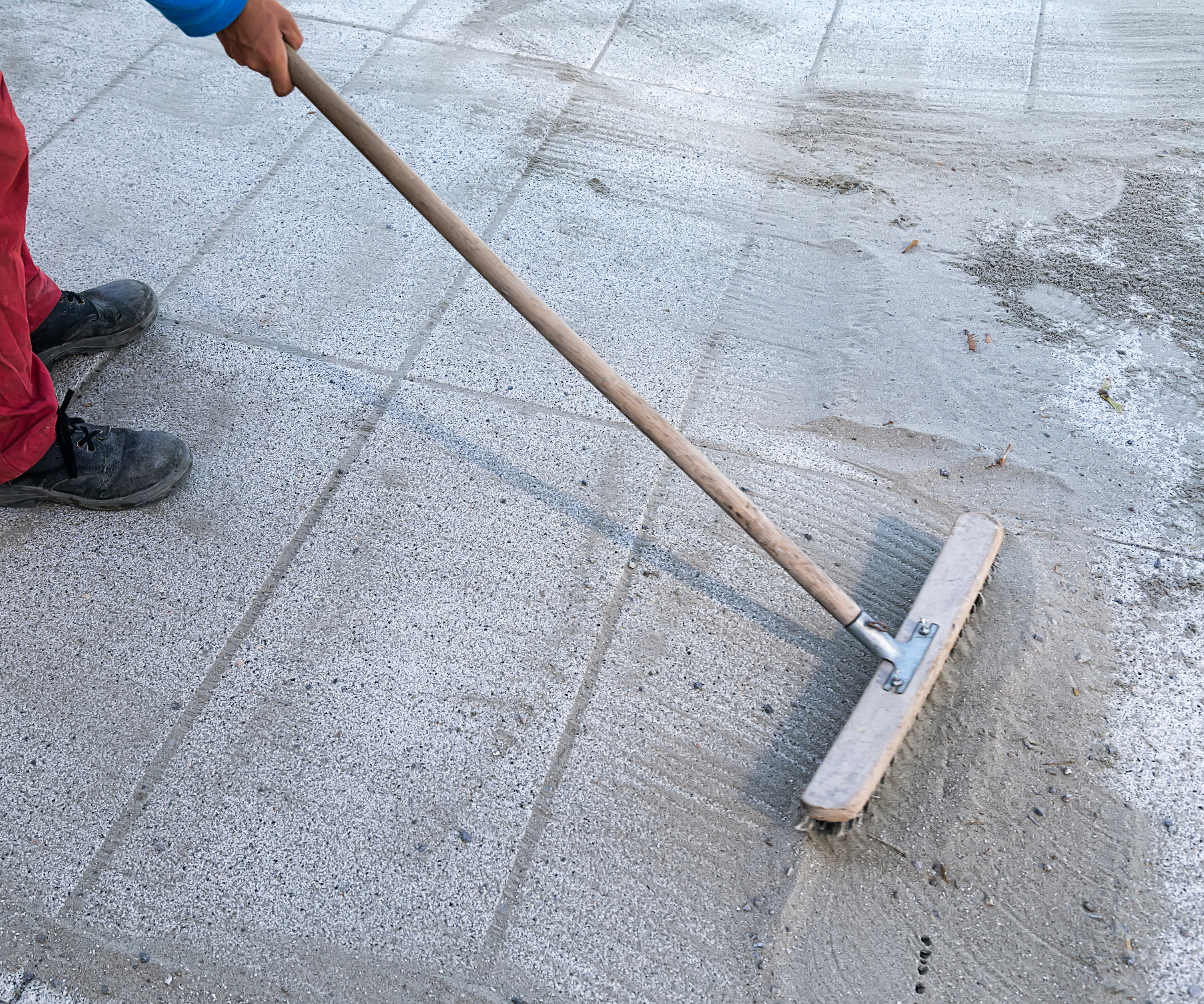 person holding broomstick which is pushing polymeric sand into the gaps between rectangular outdoor pavers
