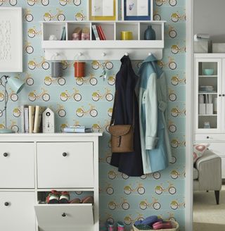 Blue wallpapered hallway with white wall-mounted shoe rack and hanging space for coats