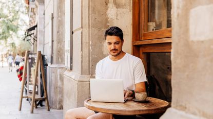 Young man working on a laptop at a sidewalk cafe in Spain