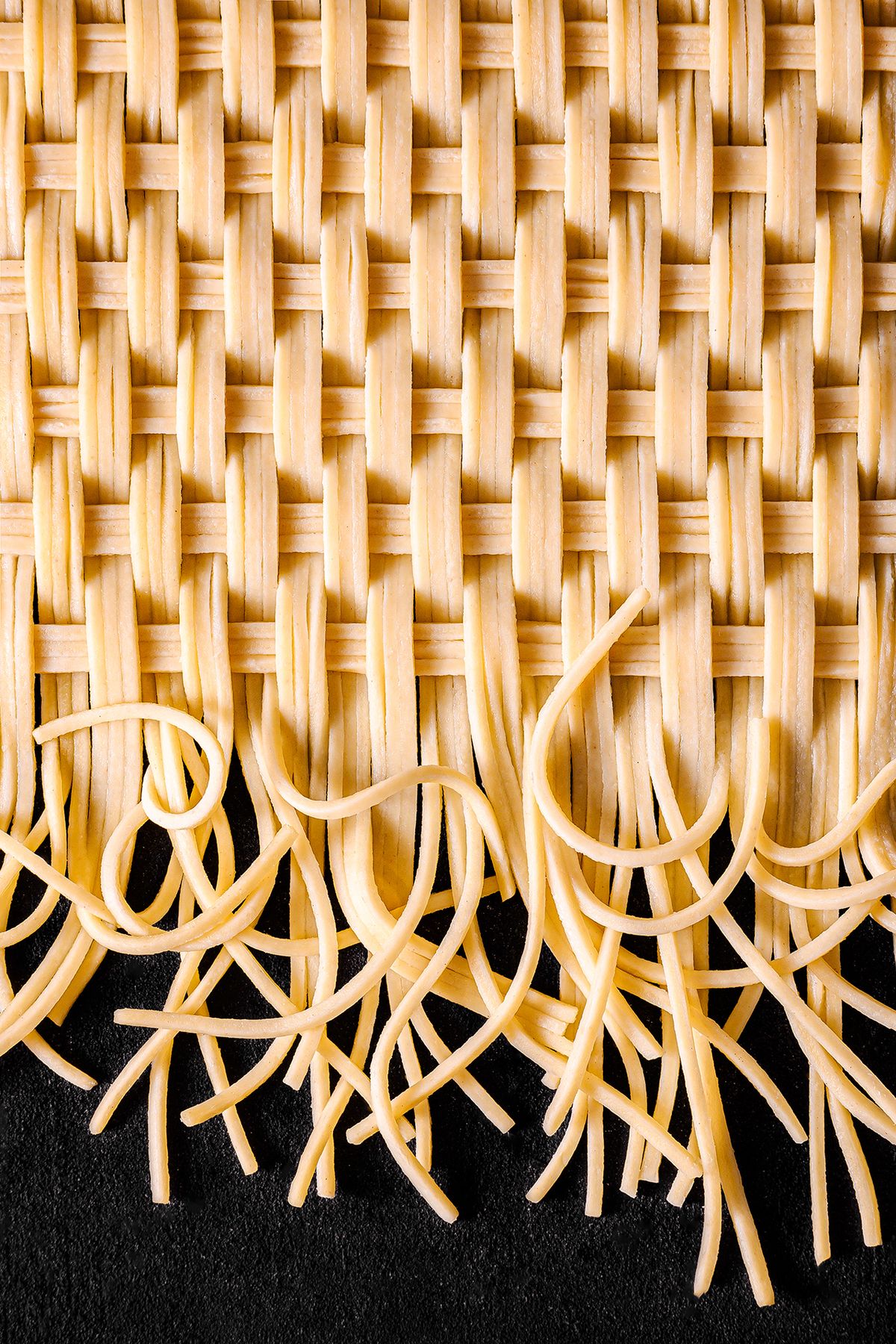 Close-up of a woven mat made of pasta, featuring long strands gracefully cascading over a dark surface