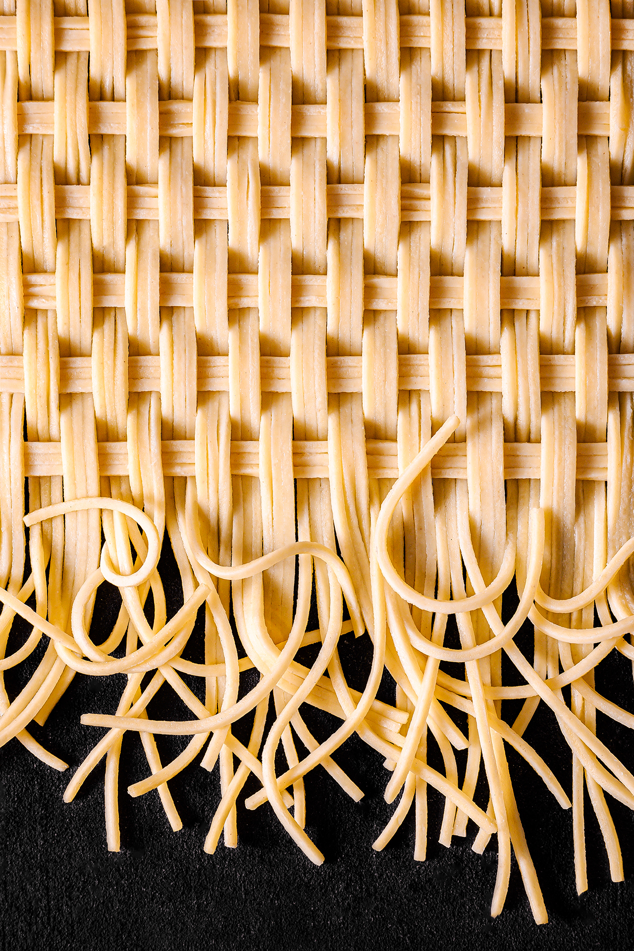 Close-up of a woven mat made of pasta, featuring long strands gracefully cascading over a dark surface