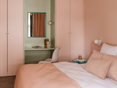 A bedroom in pastel pink with a small cabinet painte green