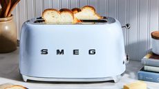 Pale blue Smeg toaster on a countertop with white bread popped up
