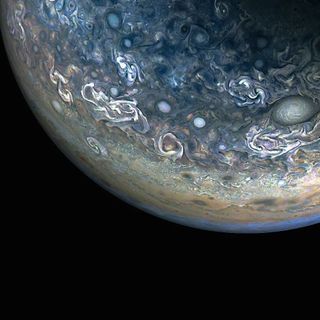 The bulbous bottom of a planetary gas giant is lit to show amazing swirls of pearly whites and blues, with laters of tans and greens and hints of pink.