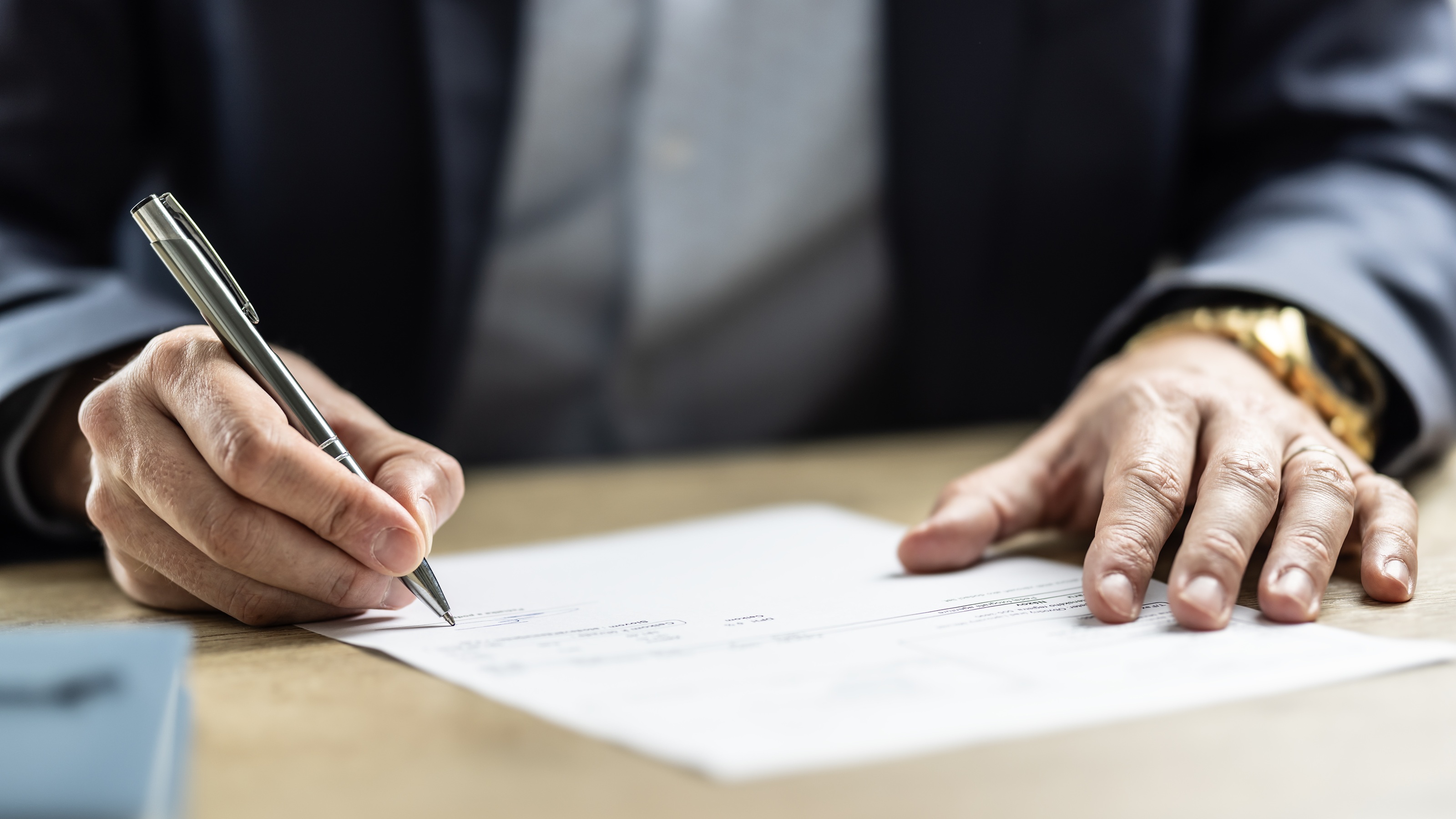 A businessman signs a document, only his hands showing.