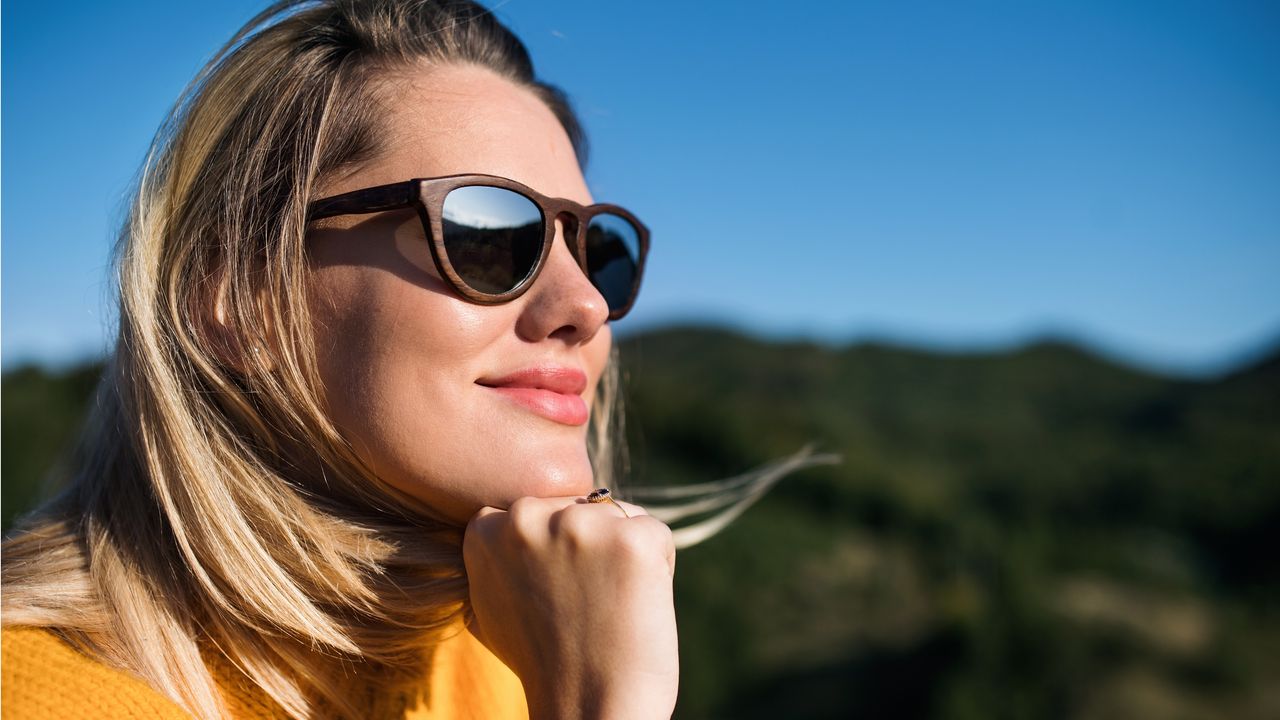 A woman wearing sunglasses smiles as she looks into the distance.