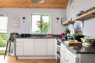 kitchen with white units black granite worktops and green window frame with wooden floor and ceiling