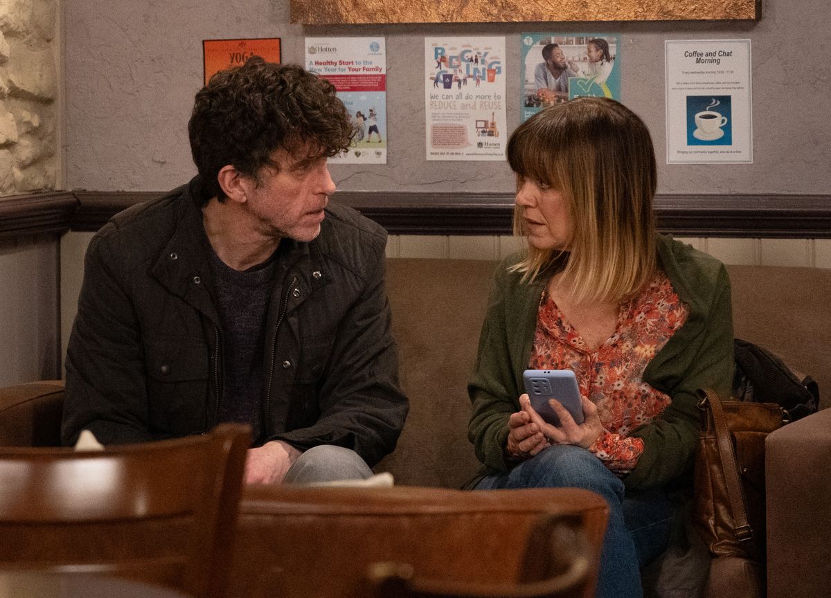 Marlon Dingle and Rhona Goskirk sit together at the cafe. Rhona is holding her phone in Emmerdale 