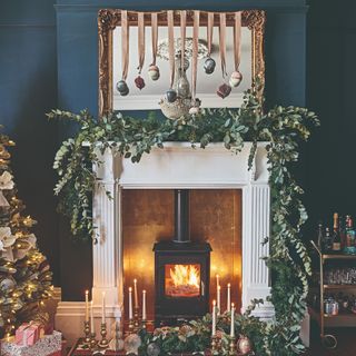 A fireplace decorated with a eucalyptus garland next to a Christmas tree