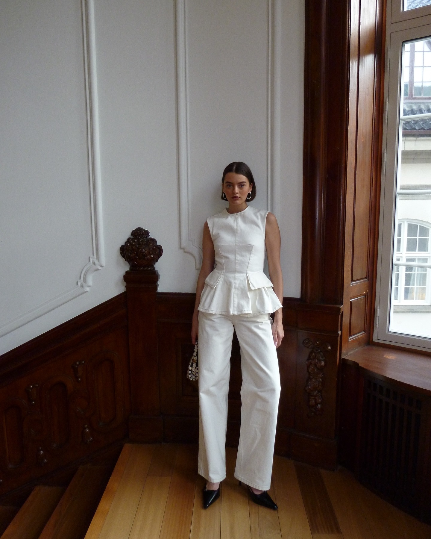 Influencer @maryljean wears a white peplum top with white jeans a black pointed-toe heels.