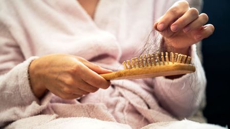 woman wearing a pink dressing gown, holding a hairbrush with clumps of dark hair