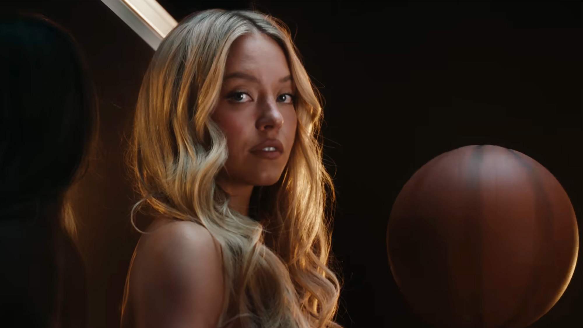 Sydney Sweeney sits on a basketball hoop and stares at the camera in viral "Just Sports" Novig ad.